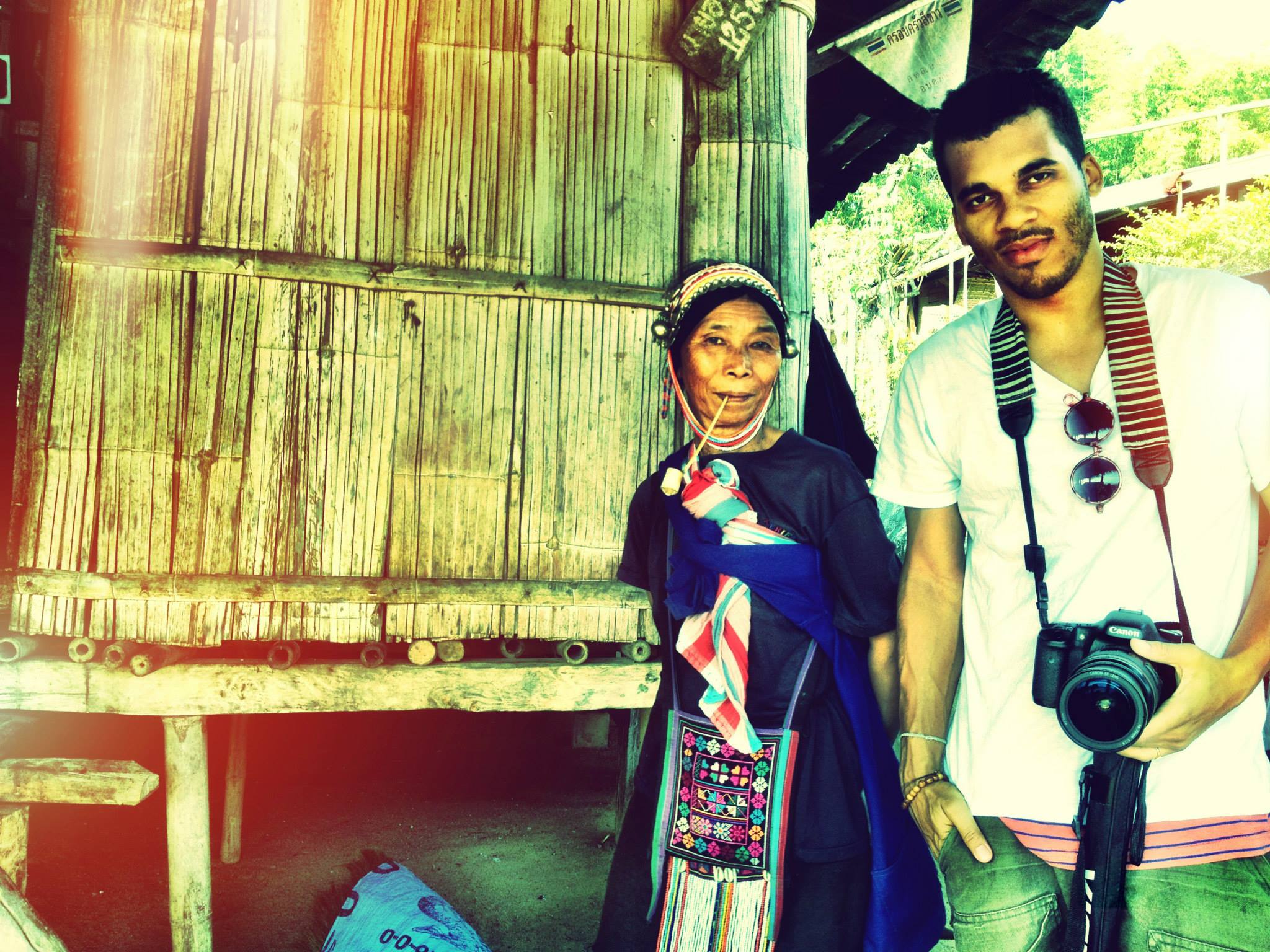 Calvin Gaskin standing beside a Thai hill-tribe elder smoking a pipe outside a bamboo house
